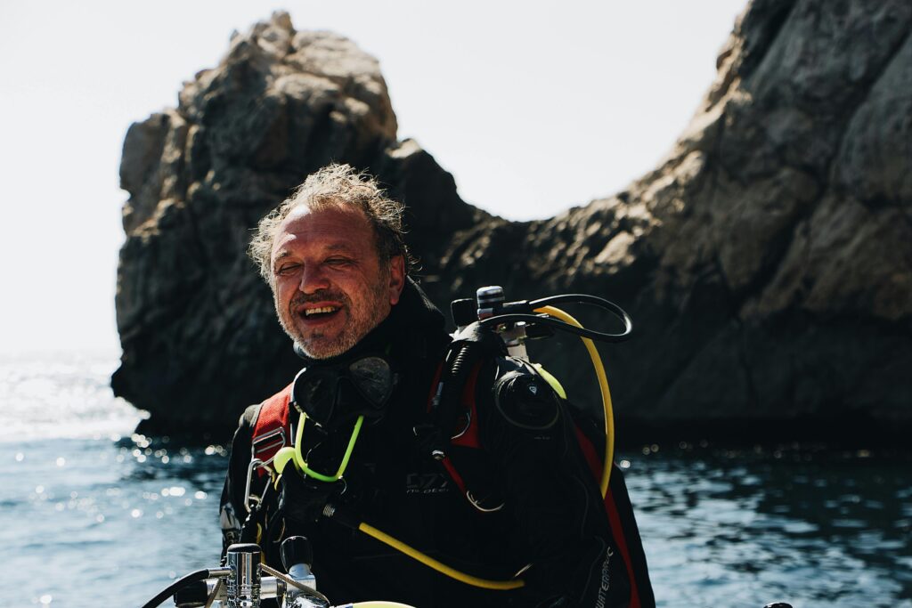 A smiling scuba diver in gear enjoys an ocean adventure near rugged rocks.